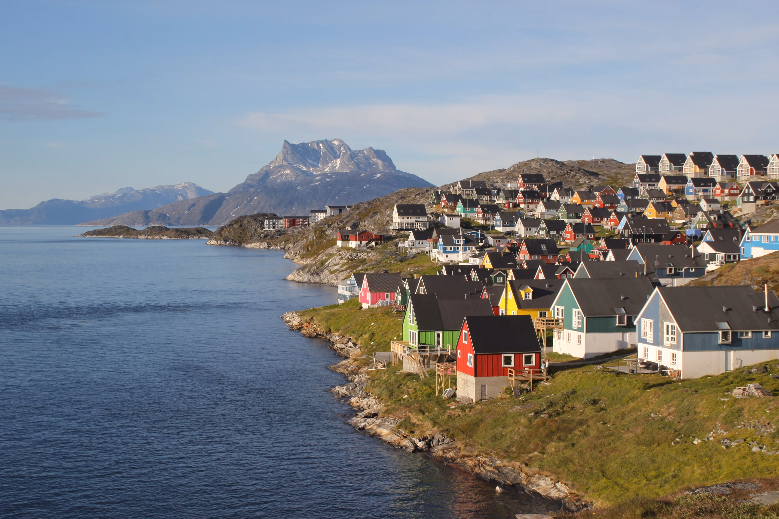 Colorful houses clustered on rocky coastline with snow-capped mountains and blue water in Greenland