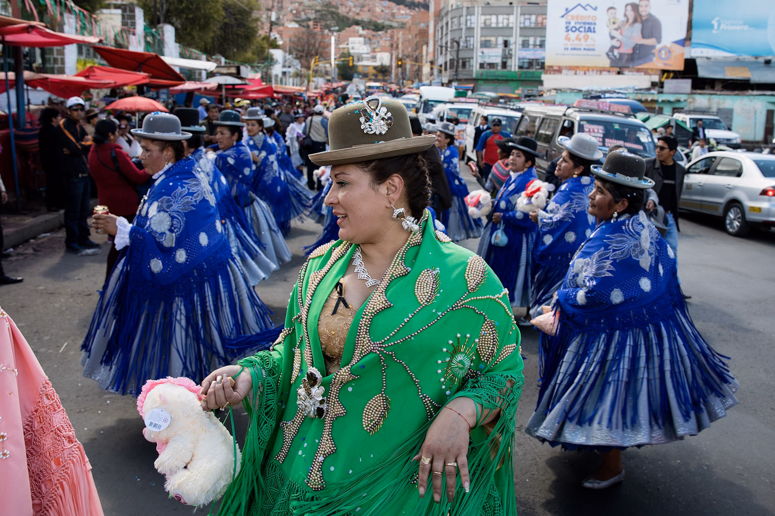 Woman in green traditional dress and bowler hat dancing at Bolivian street festival with performers