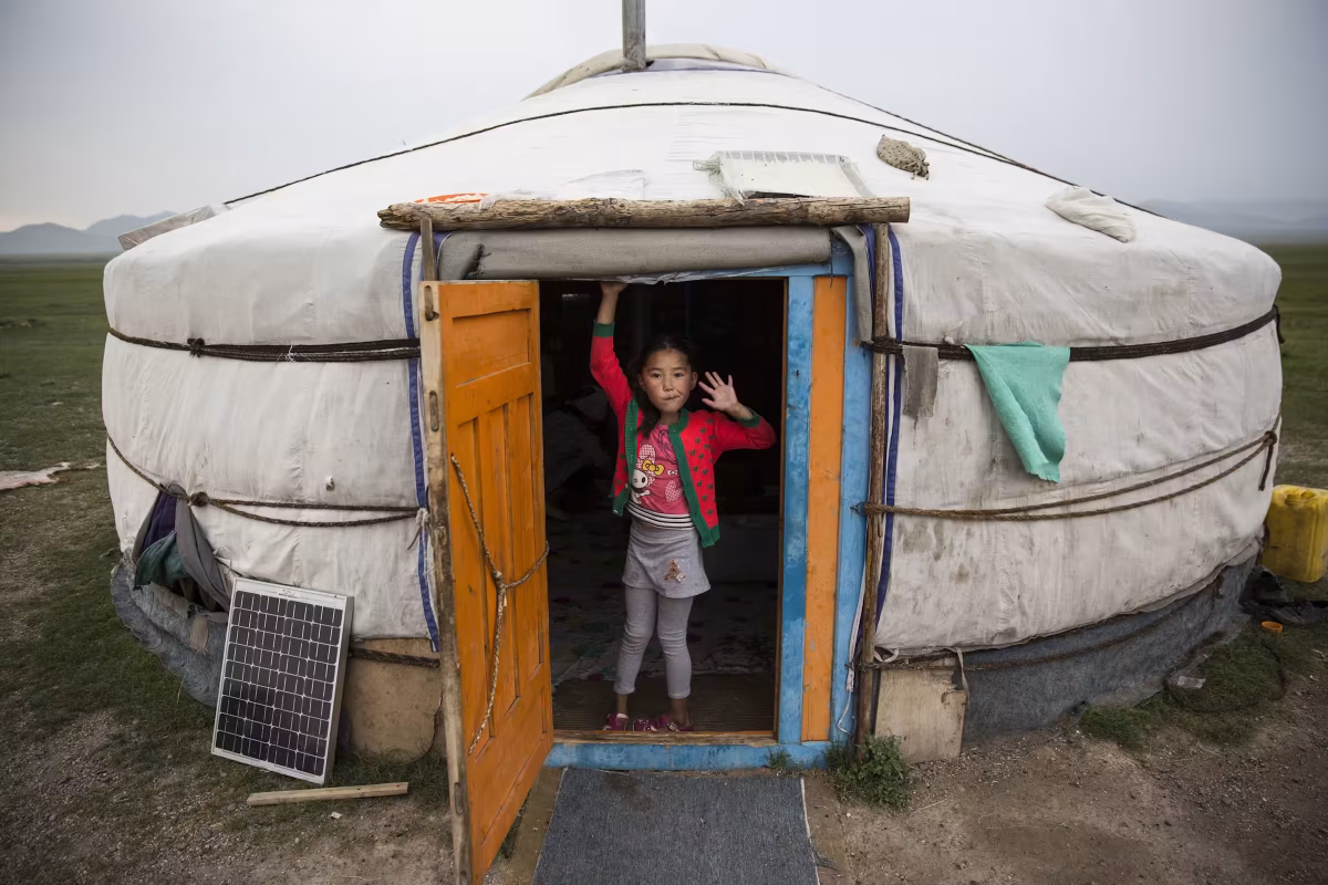 Young girl waving from doorway of traditional Mongolian yurt with solar panel on grassland steppe