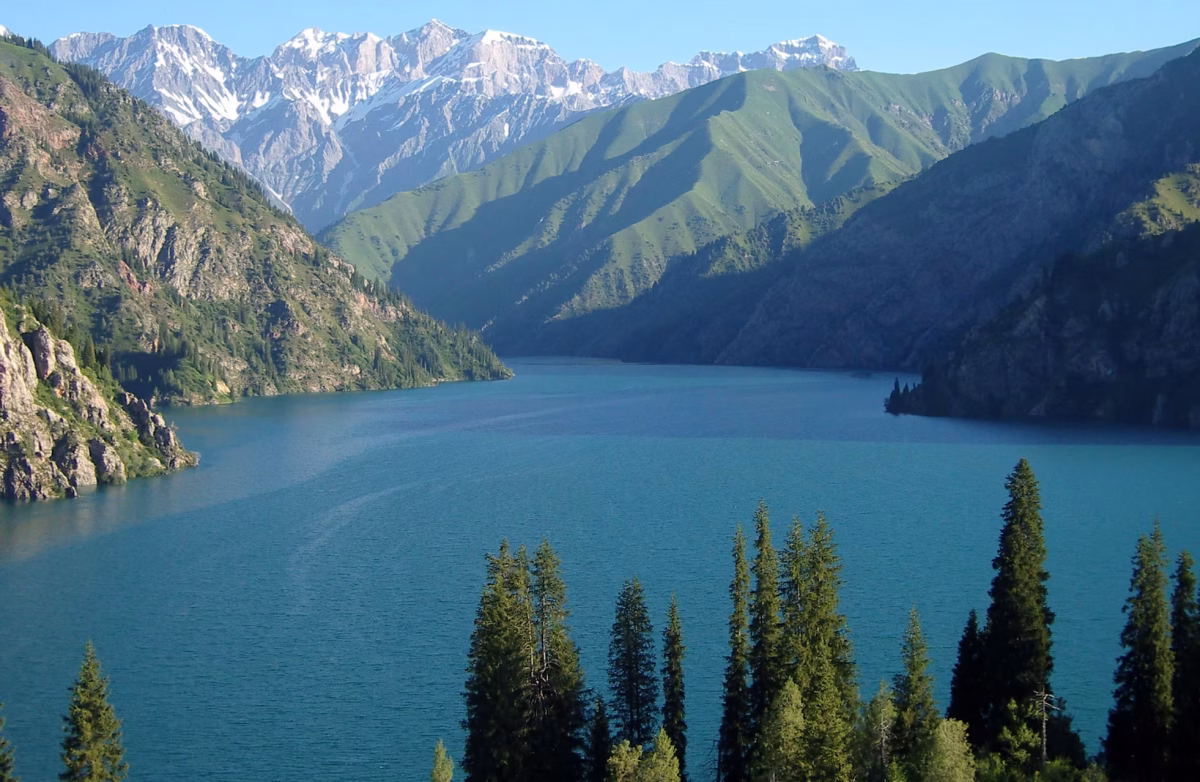 Turquoise mountain lake surrounded by snow-capped peaks and green hills in Kyrgyzstan