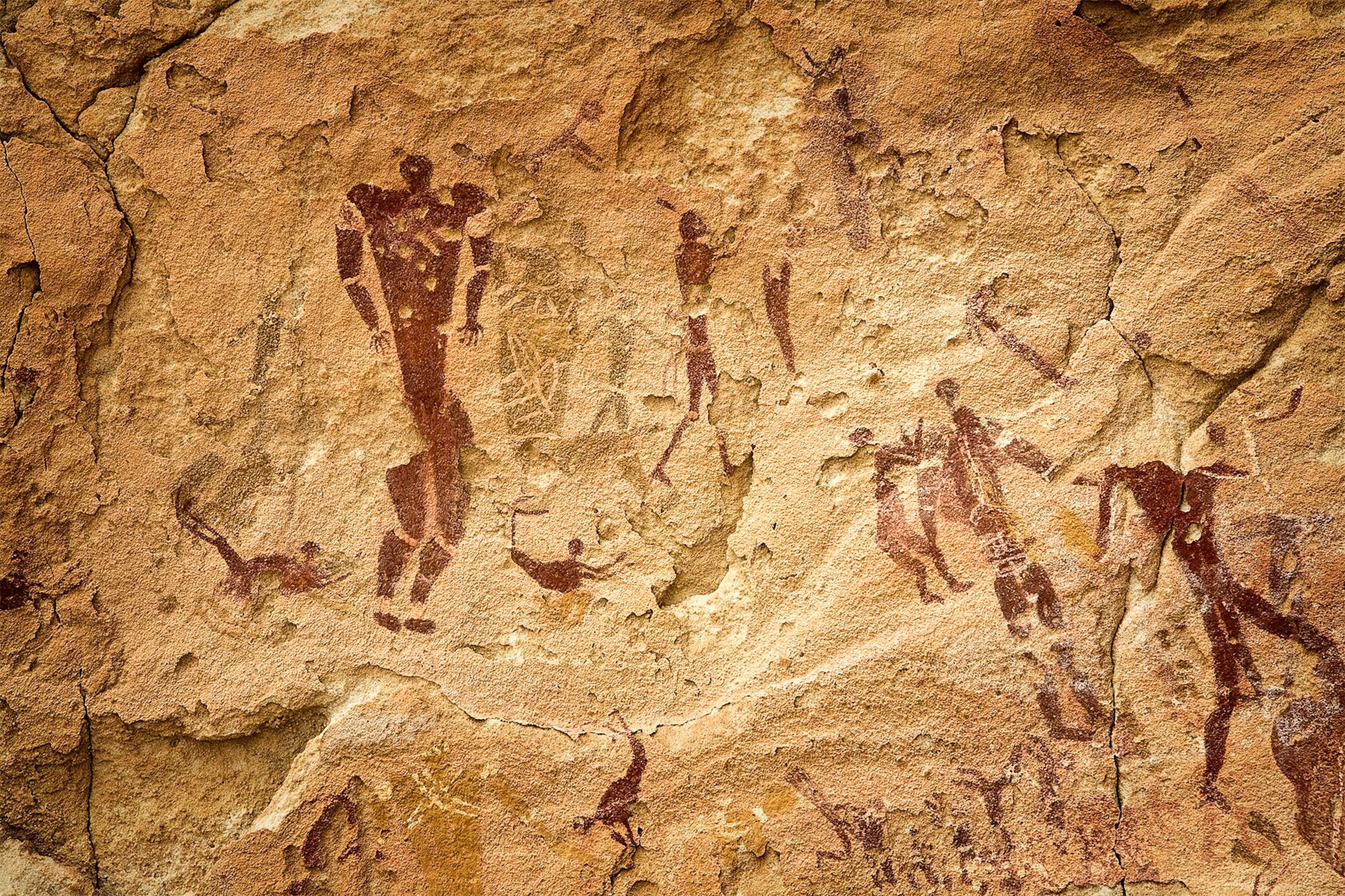 Ancient rock art cave paintings showing human figures in reddish-brown pigment on weathered sandstone wall