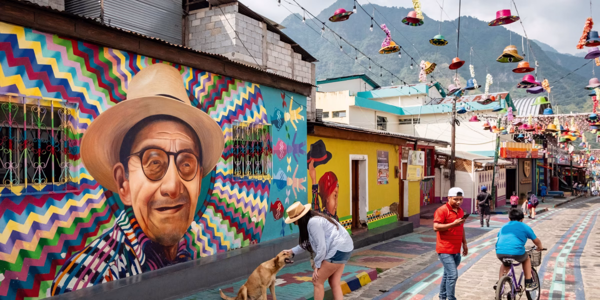 Colorful street murals and hanging hats in vibrant Guatemalan town with mountains in background