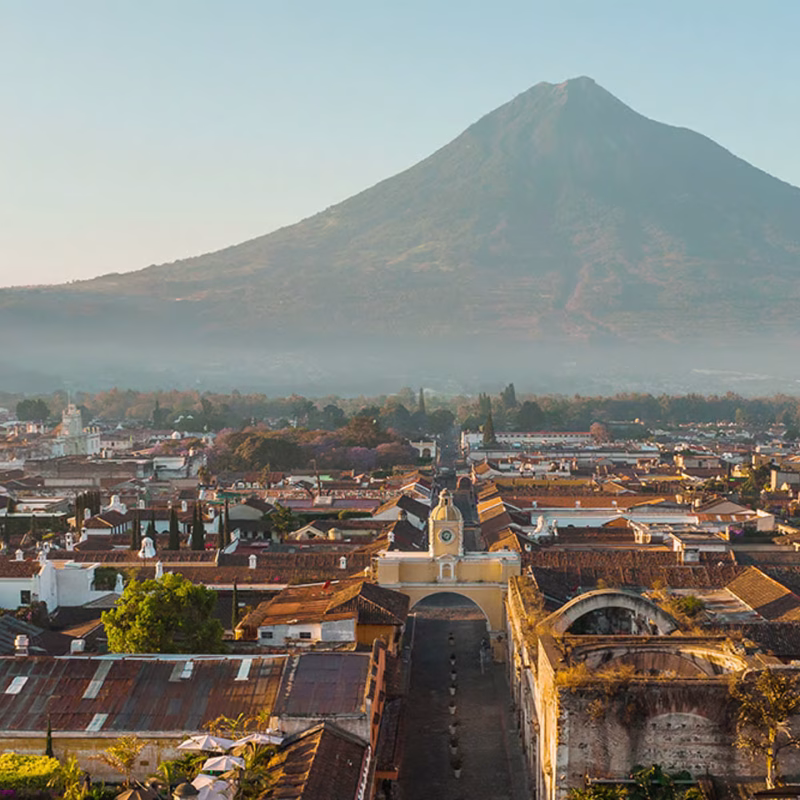 Colonial town with yellow church arch and volcano backdrop in Guatemala's golden hour light