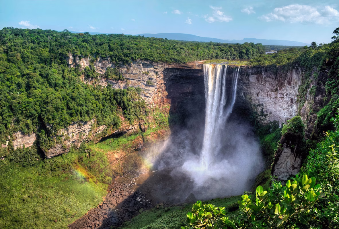 Spectacular waterfall cascading down rocky cliff with rainbow mist in lush Guyana rainforest