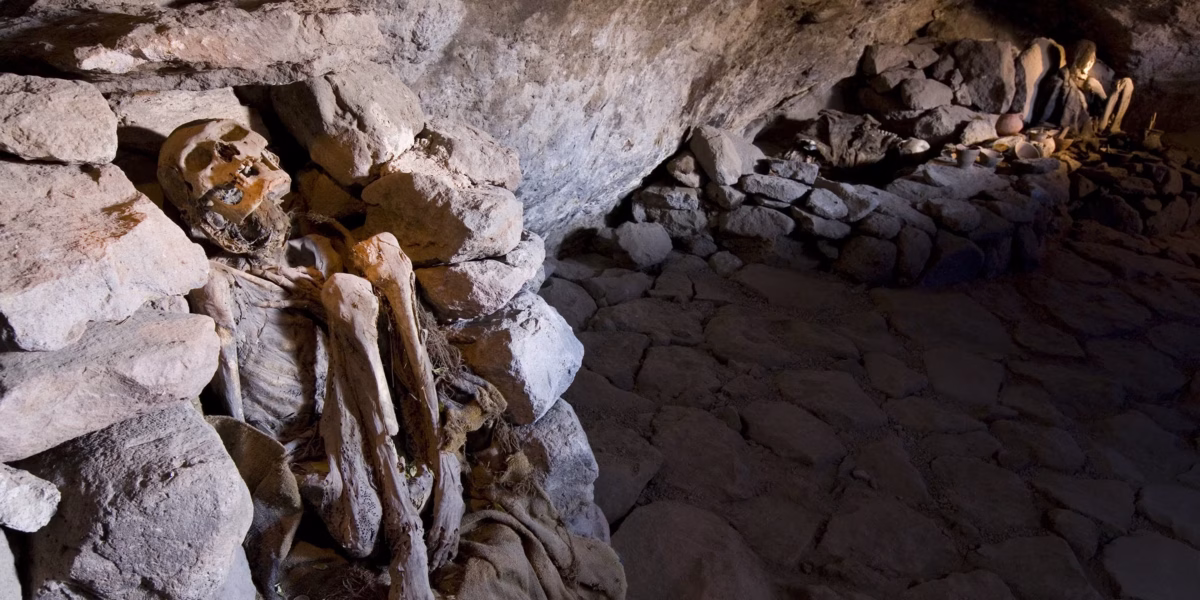 Ancient mummified remains in stone burial chamber with pottery and grave goods