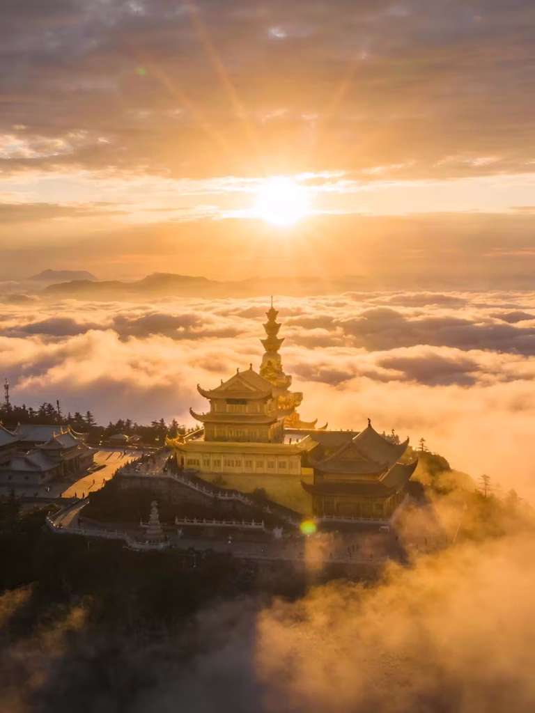 Golden temple towers on Mount Emei's summit rise above a sea of clouds under a bright sunrise