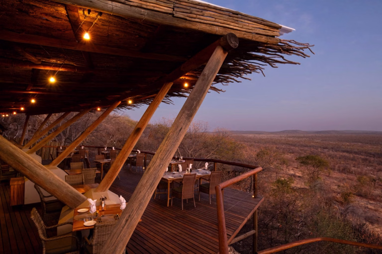 Elevated wooden dining deck at Ongava Lodge set with tables, overlooking the dry bushveld of Namibia at dusk